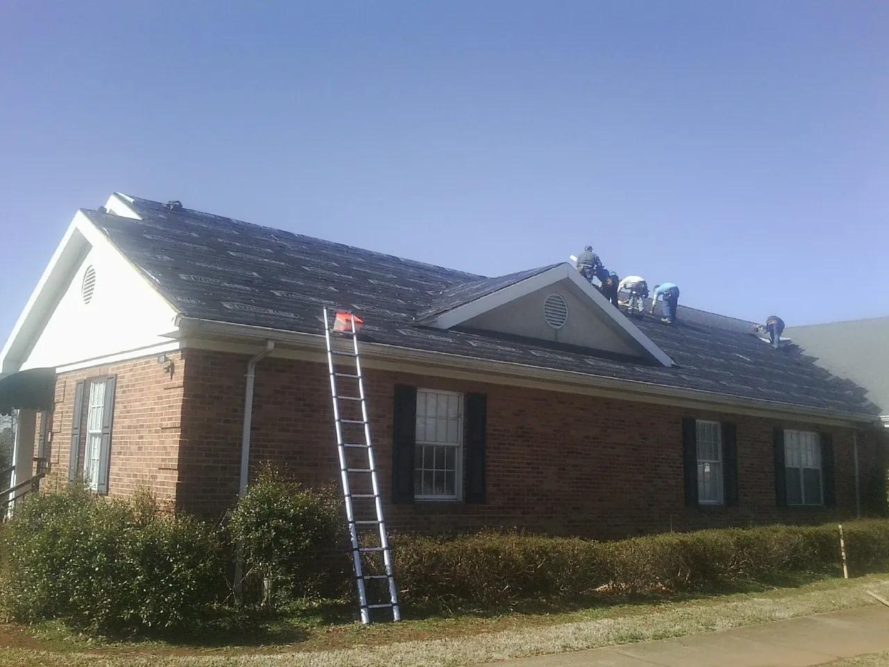 Crew tearing shingles off a brick ranch roof with a ladder set — Emergency Roof Repair work by our crew in Mays Landing