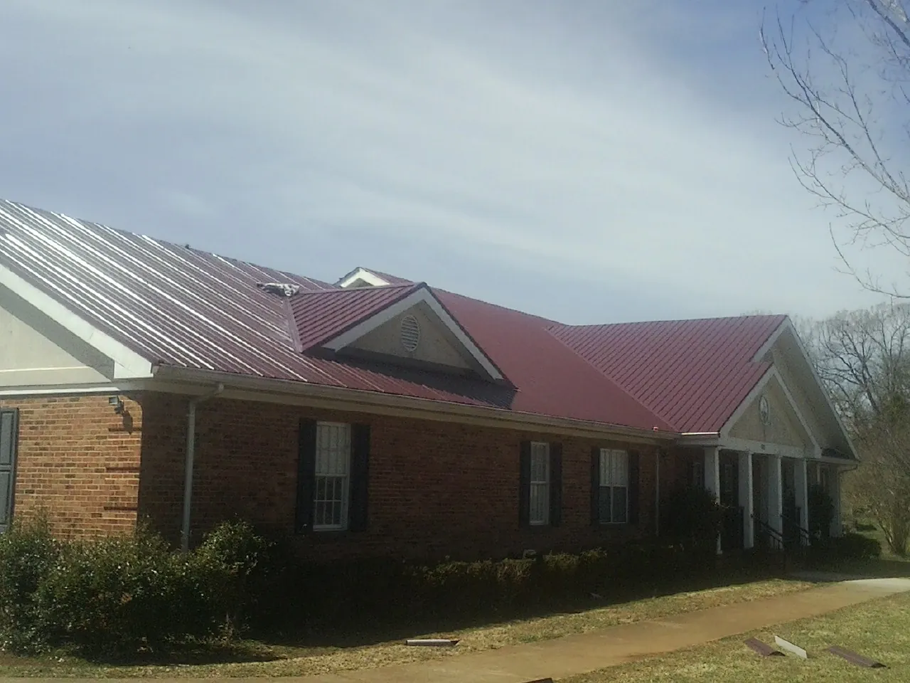 Red metal roof with gabled entries on a long brick building, from a Hail Damage Roof Repair job in Mays Landing