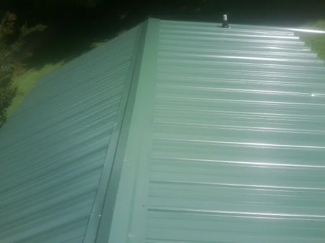 New green metal panels meeting at the ridge of a roof — Flat Roof Repair work by our crew in Mays Landing
