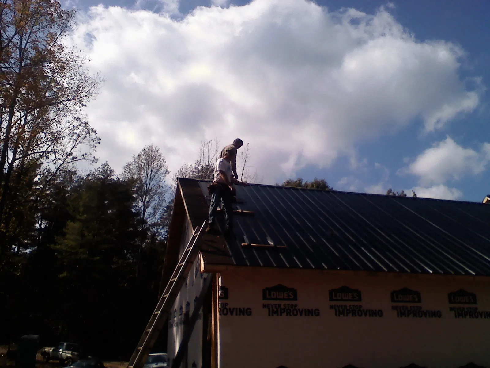 Roofer fastening dark metal panels high against a cloudy sky, from a Roof Inspection job in Mays Landing