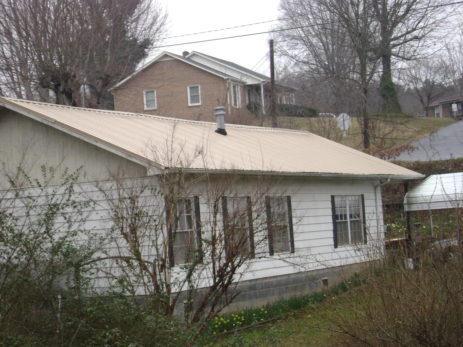 Tan metal roof on a white sided house set into a hillside — Commercial Roofing by Roofing Brothers in Mays Landing